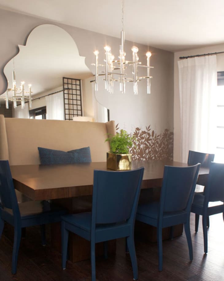 Dining room with blue chairs, wooden table, beige bench, chandelier, and decorative wall mirror.