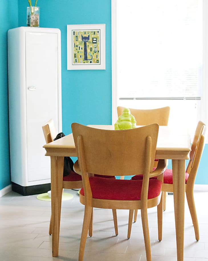 Dining area with wooden table, red cushioned chairs, turquoise wall, and white cabinet.
