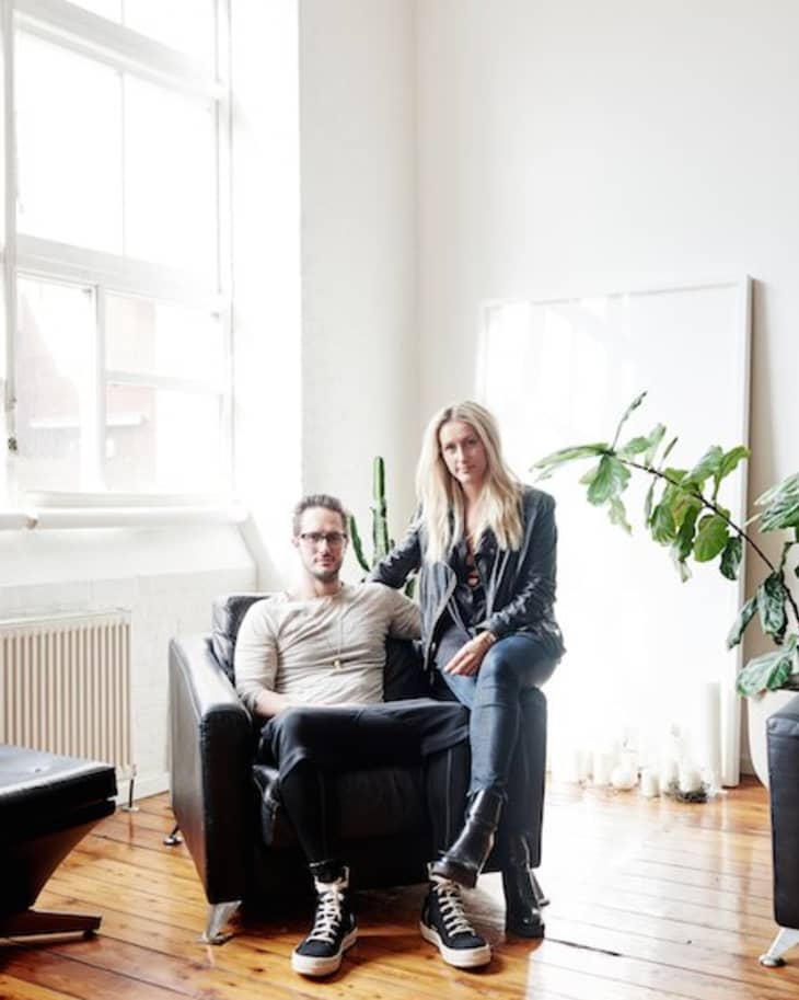 Man sitting and woman standing in a bright room with leather chair, large window, and potted plant.