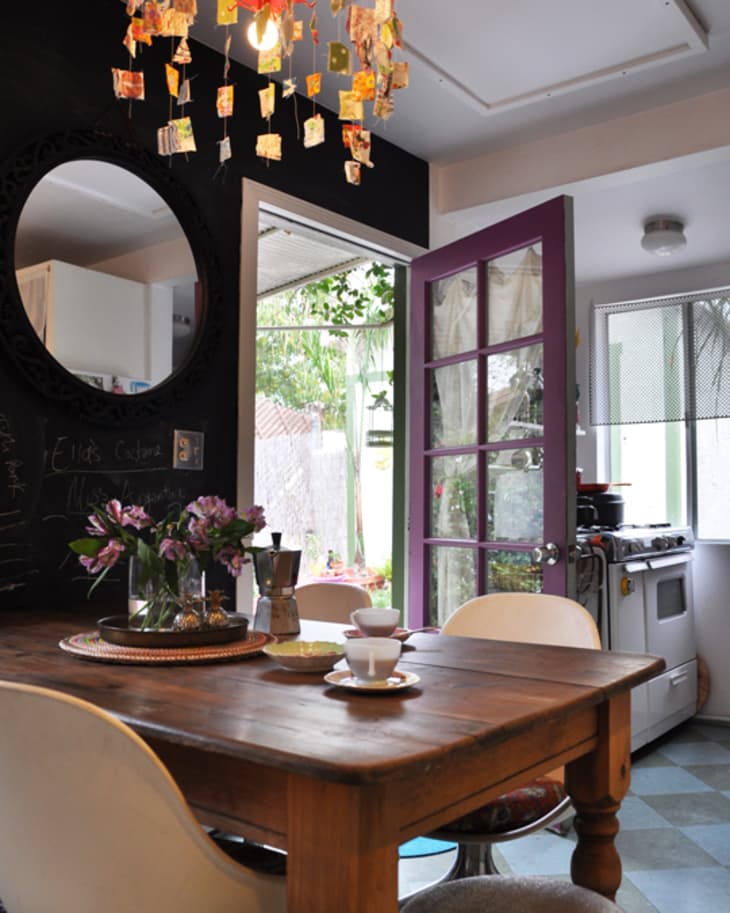 Cozy kitchen with wooden table, purple door, colorful chandelier, and flowers in a vase.