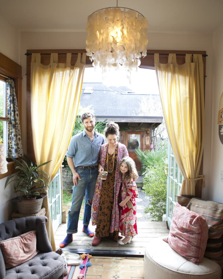 Family standing in doorway with yellow curtains, patterned rug, and cozy living room decor.