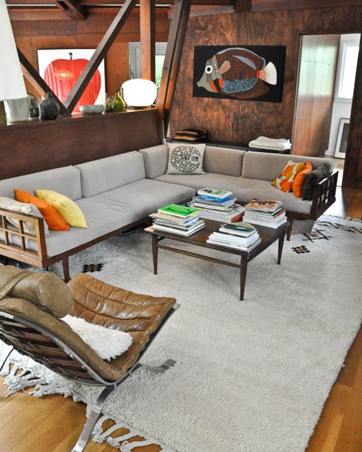 Mid-century modern living room with gray sectional sofa, colorful pillows, leather chair, and coffee table stacked with books.