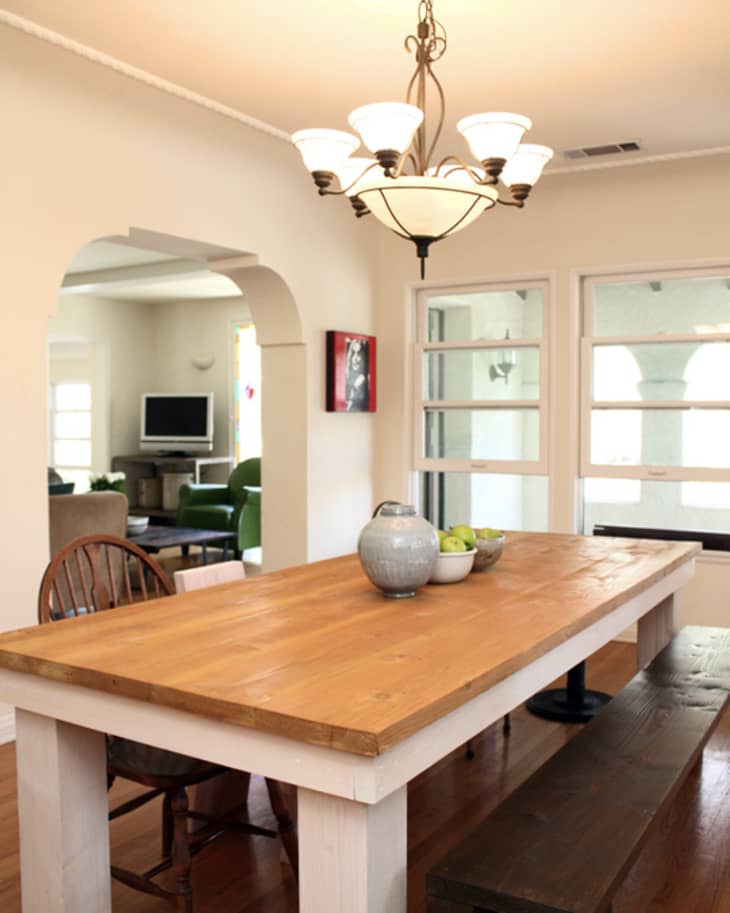 Dining room with wooden table, bench, chairs, chandelier, and view into living room with TV and green chair.