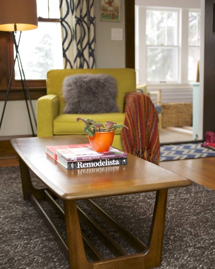 Mid-century modern living room with a yellow armchair, wooden coffee table, books, and a plant in an orange pot.