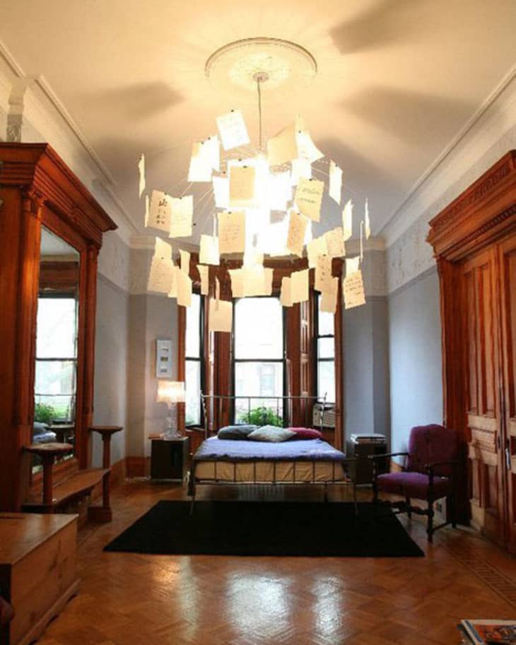 Bedroom with a unique chandelier of hanging notes, wooden furniture, and a metal bed frame near large windows.