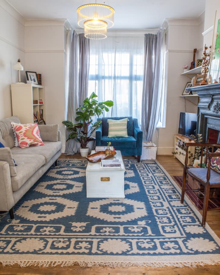 Living room with a gray sofa, blue armchair, patterned rug, white coffee table, and potted plant by a window.