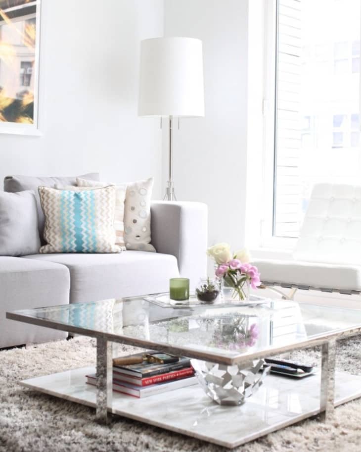A square coffee table with plants stacked on top and books stacked on the bottom shelf