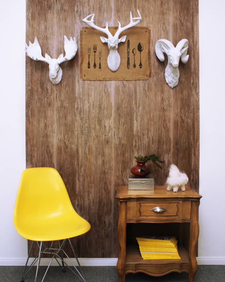 Yellow chair and wooden side table with decor against a wood-paneled wall featuring white animal head sculptures.