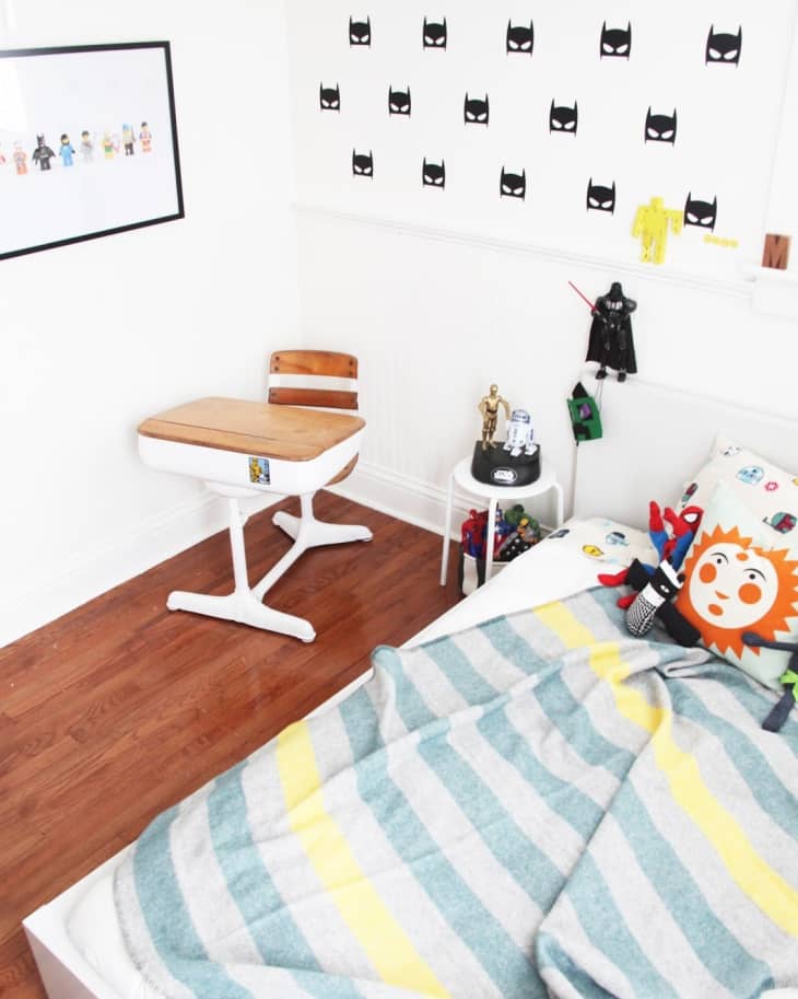 Kids' room with superhero-themed decor, Batman wall stickers, a wooden desk, and a bed with a striped blanket.