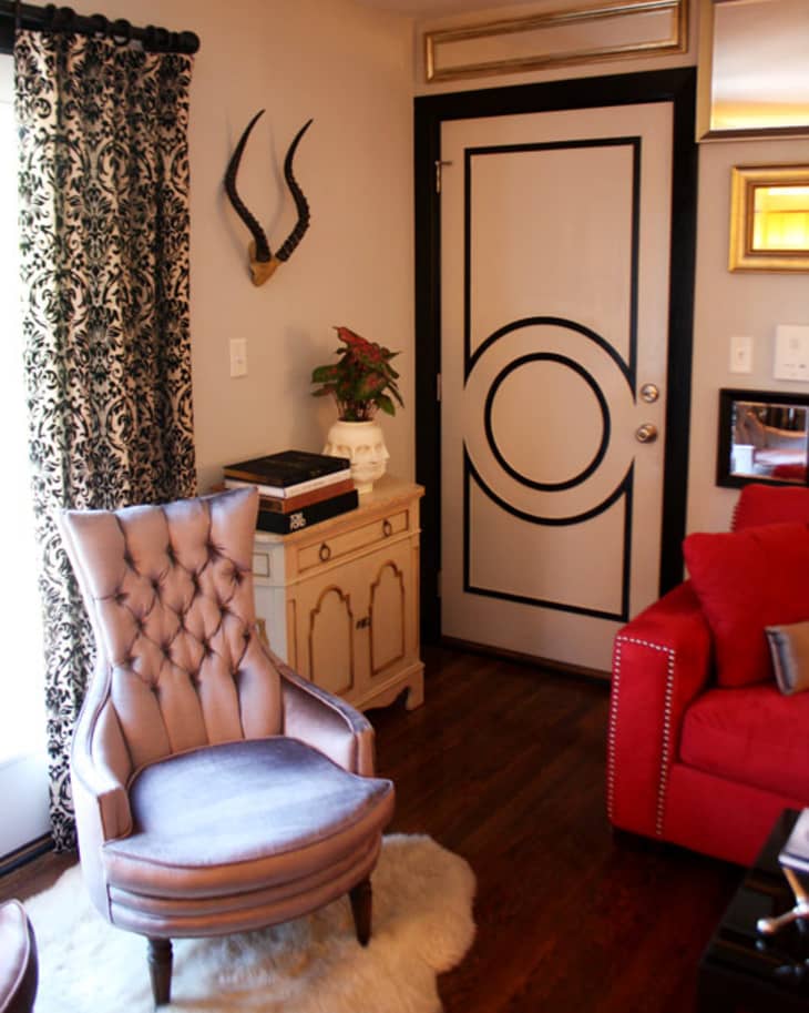 Cozy living room with tufted chair, red sofa, ornate door, and decorative antlers on the wall.