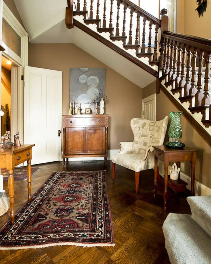 Staircase hallway with wooden furniture, patterned rug, armchair, and decorative vase on a side table.