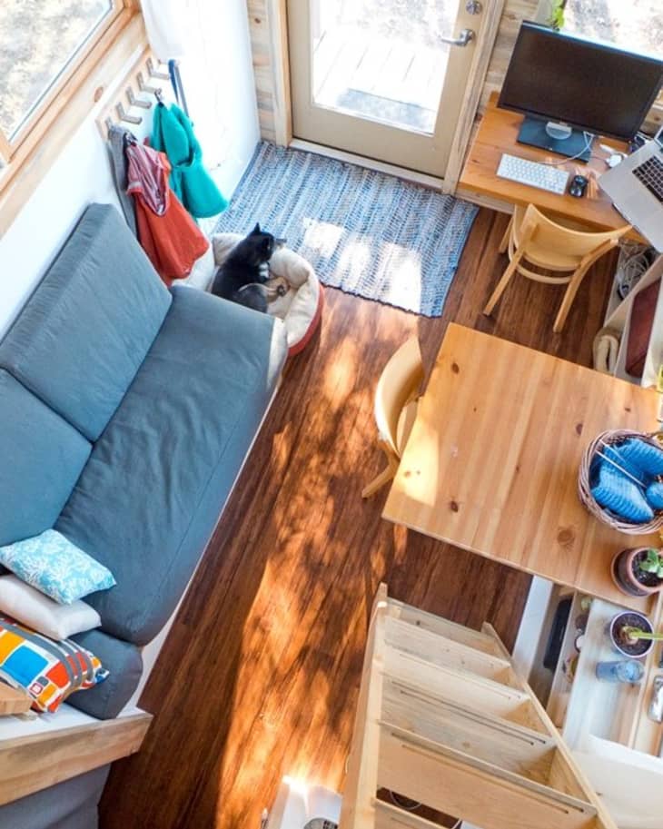 Cozy tiny home interior with a blue sofa, wooden table, desk with computer, and a dog in a bed by the door.