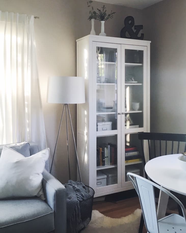 Cozy living room with a gray sofa, white cabinet, floor lamp, and round dining table with chairs.