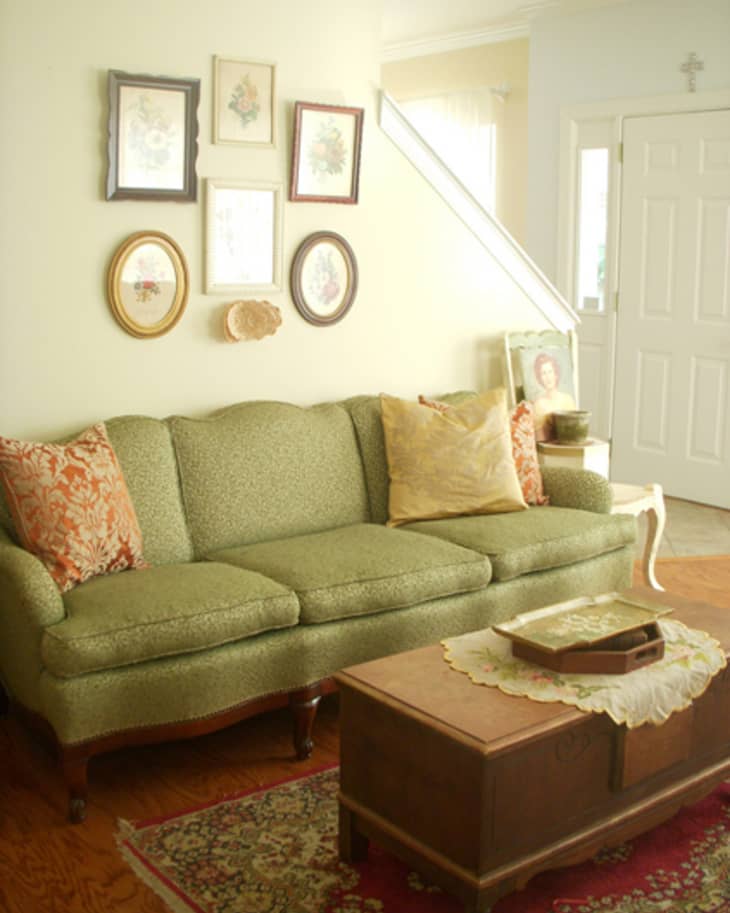 Living room with green sofa, floral cushions, wooden coffee table, and framed art on the wall.