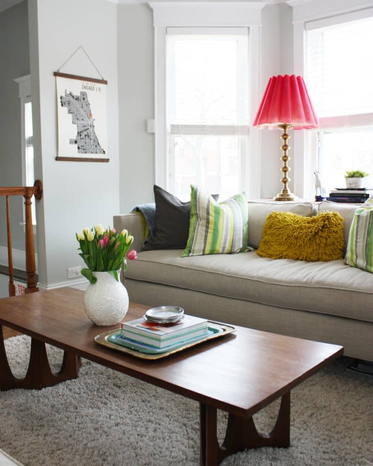 Living room with a beige sofa, colorful pillows, red lamp, wooden coffee table, and vase of tulips.