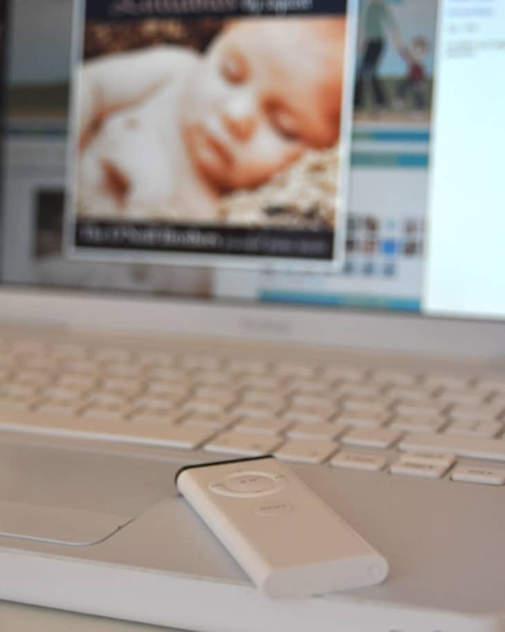 Laptop with a white remote on the keyboard, displaying a blurred image of a sleeping baby on the screen.