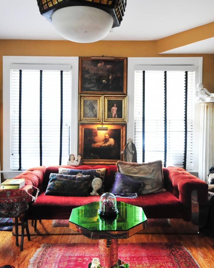 Eclectic living room with red sofa, colorful pillows, vintage paintings, and a green mirrored table on a red patterned rug.
