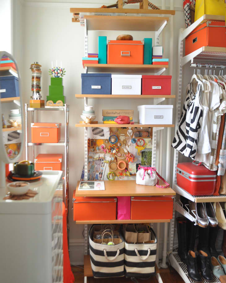 Organized closet with colorful storage boxes, hanging clothes, striped baskets, and a corkboard with pinned items.