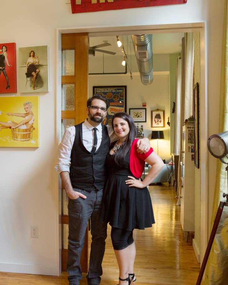 Couple standing under a "Pin-Ups" sign in a hallway with pin-up art on the walls.