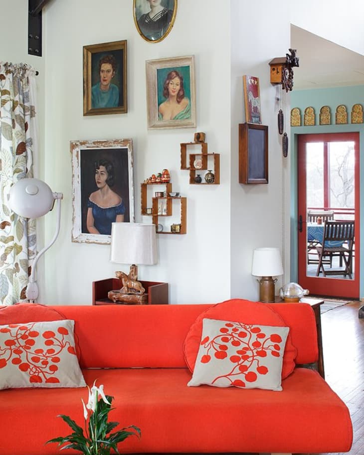 Red sofa with floral cushions, wall art, and a potted plant in a cozy living room with a view of a red-framed door.