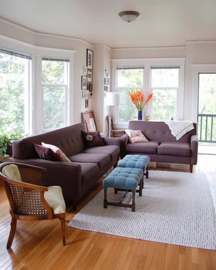Living room with two brown sofas, blue tufted bench, wooden chair, and vase of orange flowers on a side table.