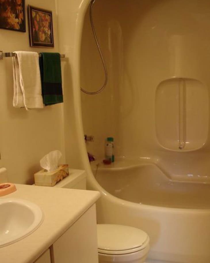 Beige bathroom with a curved shower-tub combo, white sink, and towels on a rack.