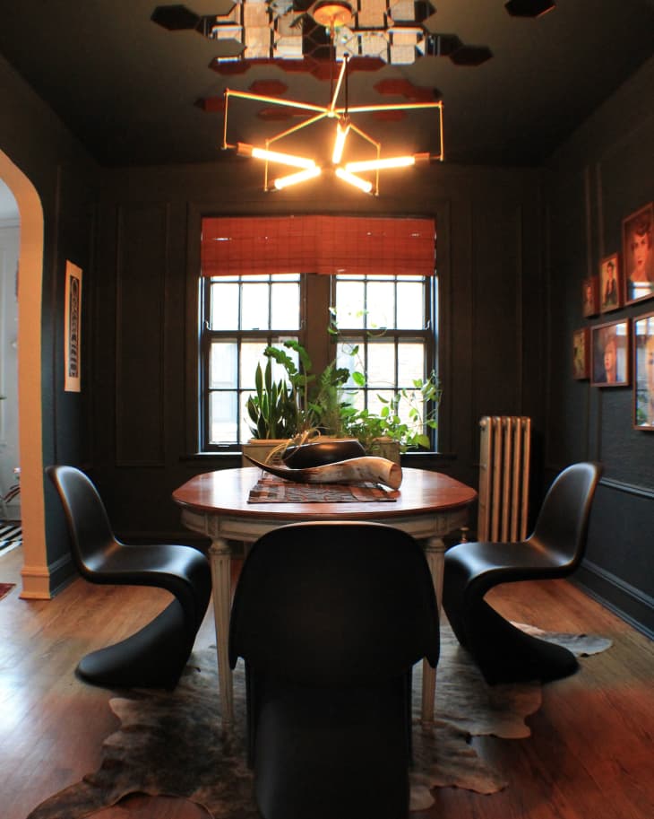 Dining room with black chairs, wooden table, modern chandelier, and plants by the window.