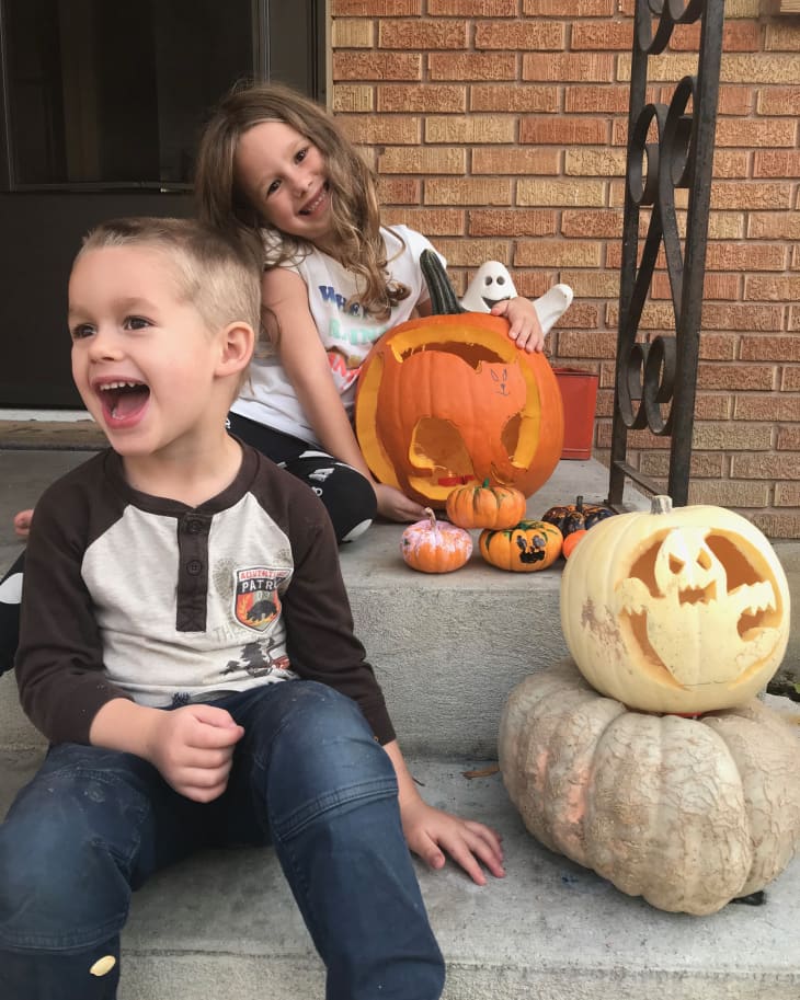 Two children sitting on steps with carved pumpkins and small painted pumpkins for Halloween.