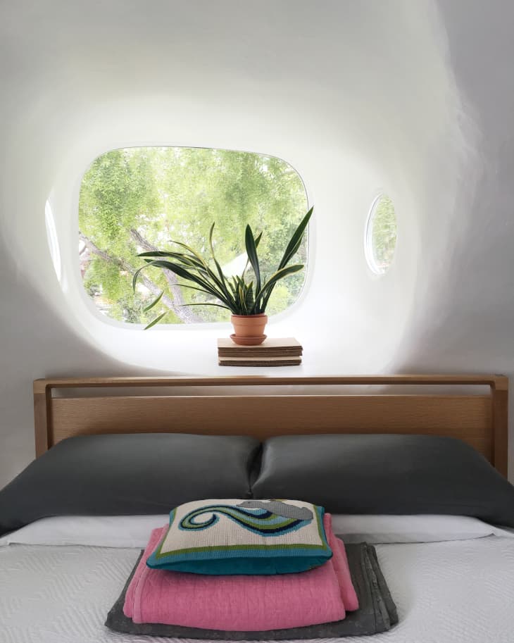Modern bedroom with a wooden headboard, gray pillows, and a potted plant on a windowsill.