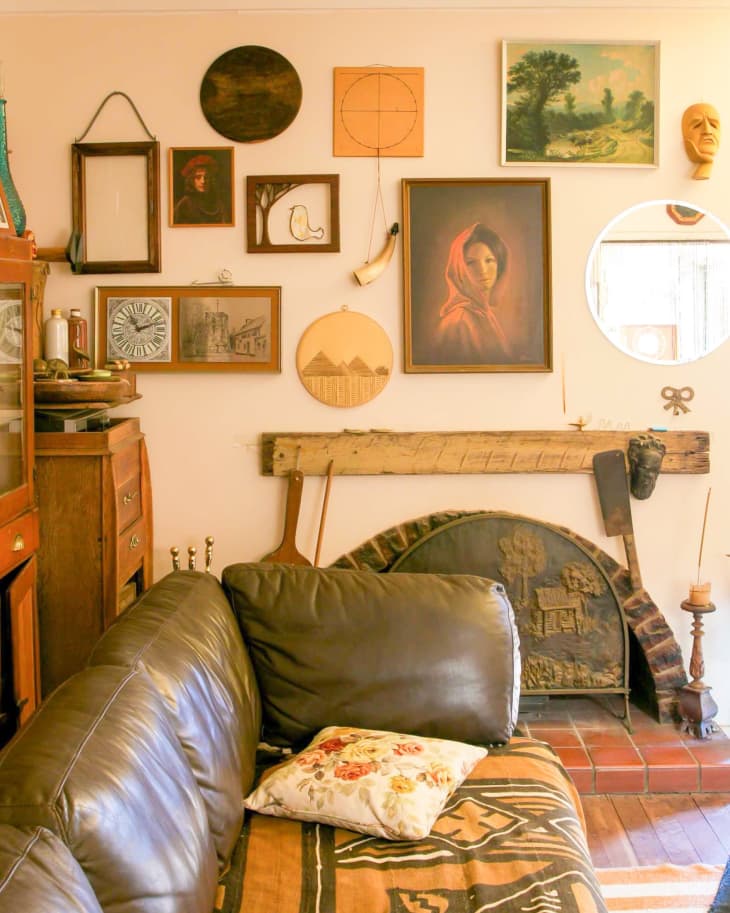 Living room with brown leather sofa, floral pillow, eclectic wall art, and a rustic fireplace.