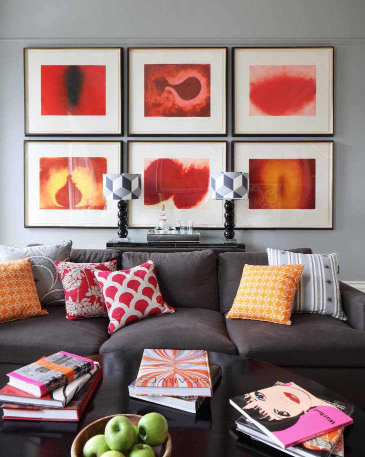 Gray sofa with colorful pillows, abstract red art on wall, books, and a bowl of green apples on a black coffee table.