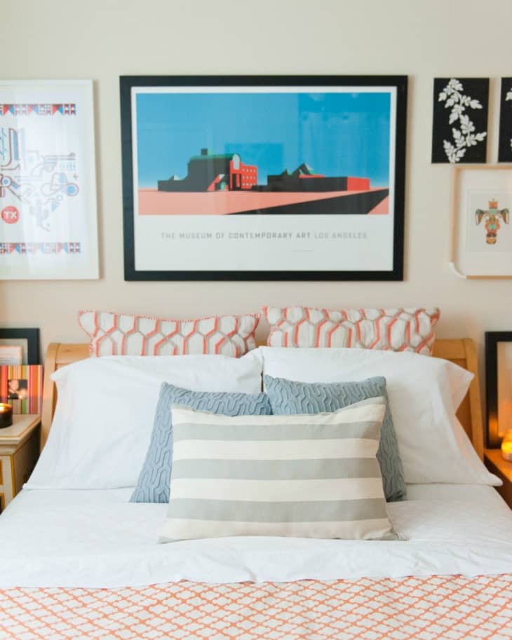 Bed with patterned pillows, striped cushion, and art prints on the wall, including a Museum of Contemporary Art Los Angeles poster.