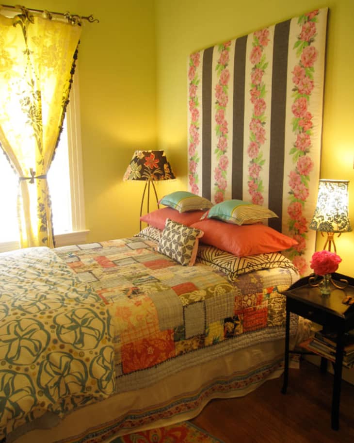 Colorful bedroom with floral headboard, patchwork quilt, patterned pillows, and decorative lamps on bedside tables.