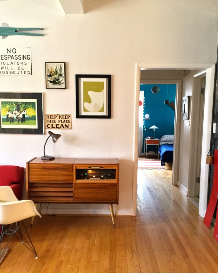 Mid-century modern living room with wooden console, wall art, and view into a blue-walled bedroom.
