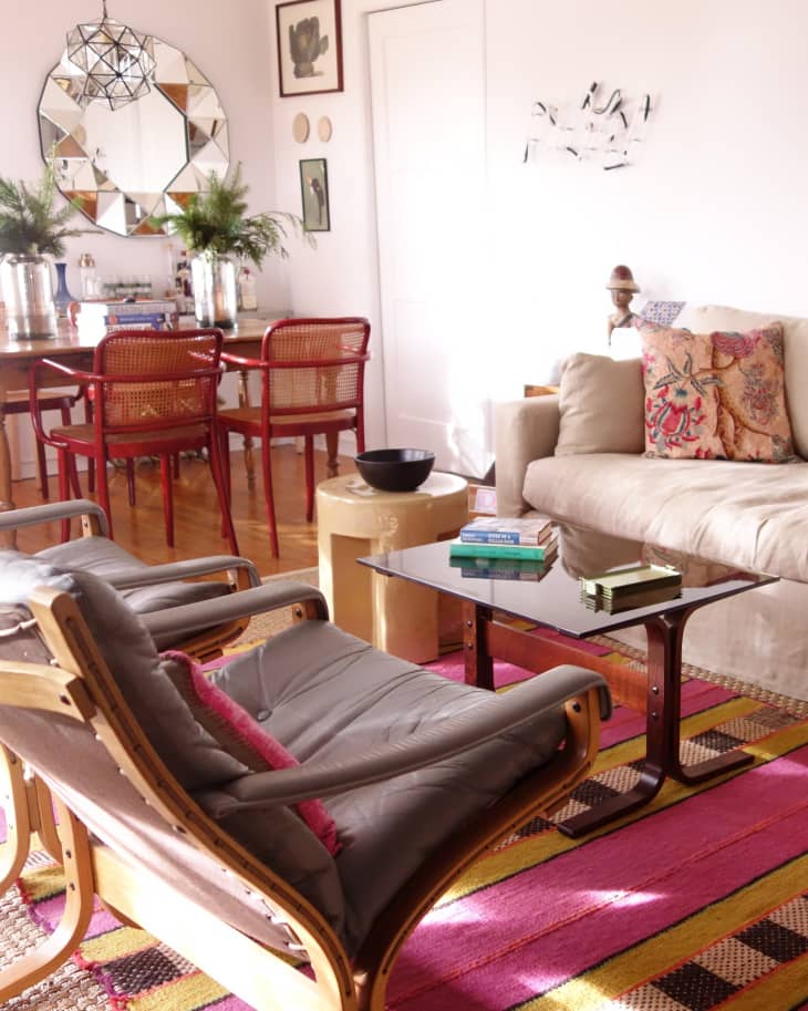 Living room with beige sofa, colorful rug, glass coffee table, and red dining chairs near a mirrored wall.