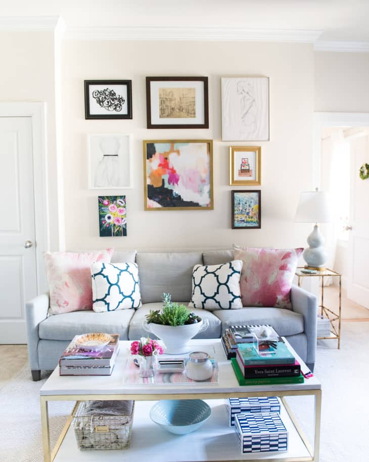 Living room with a gray sofa, pink and blue pillows, a gold coffee table, and a gallery wall of framed art.