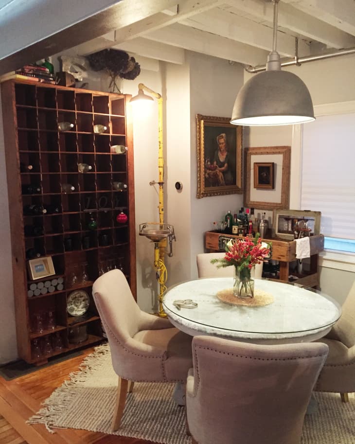 Dining area with round marble table, beige chairs, wine rack, and framed artwork on the wall.