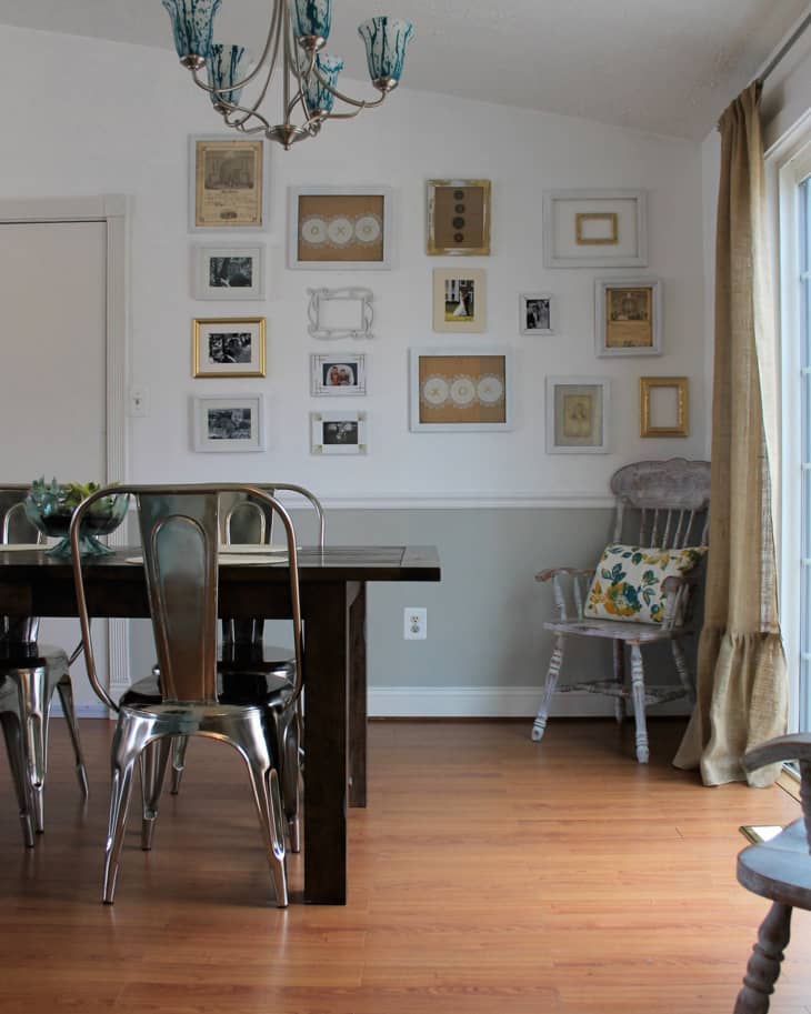 Dining room with dark wood table, metal chairs, gallery wall, chandelier, and a rocking chair with a floral cushion.