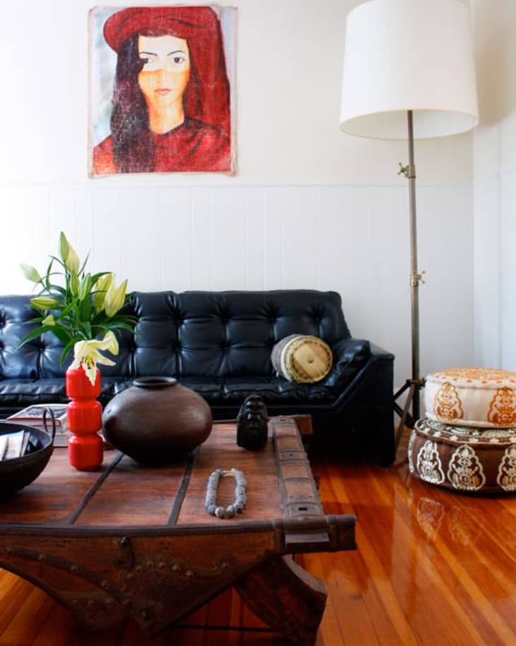 Living room with black leather sofa, wooden coffee table, large floor lamp, and a colorful portrait on the wall.