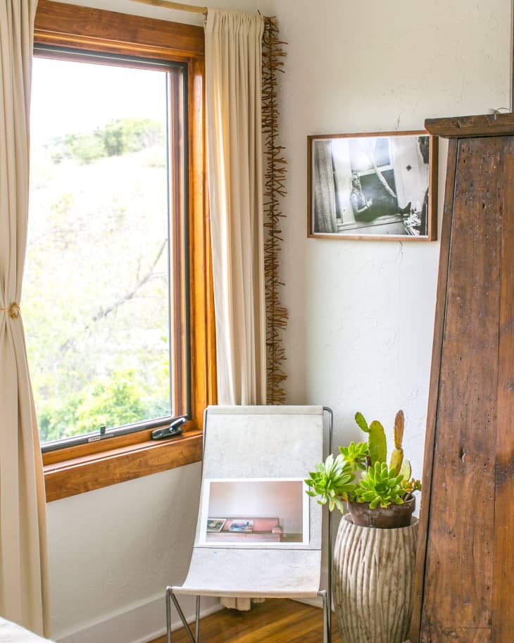 Chair with a framed photo, next to a large potted succulent and a wooden wardrobe, by a window with cream curtains.