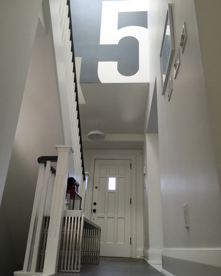 Narrow hallway with white door, metal bench, and large number 5 painted on the ceiling.