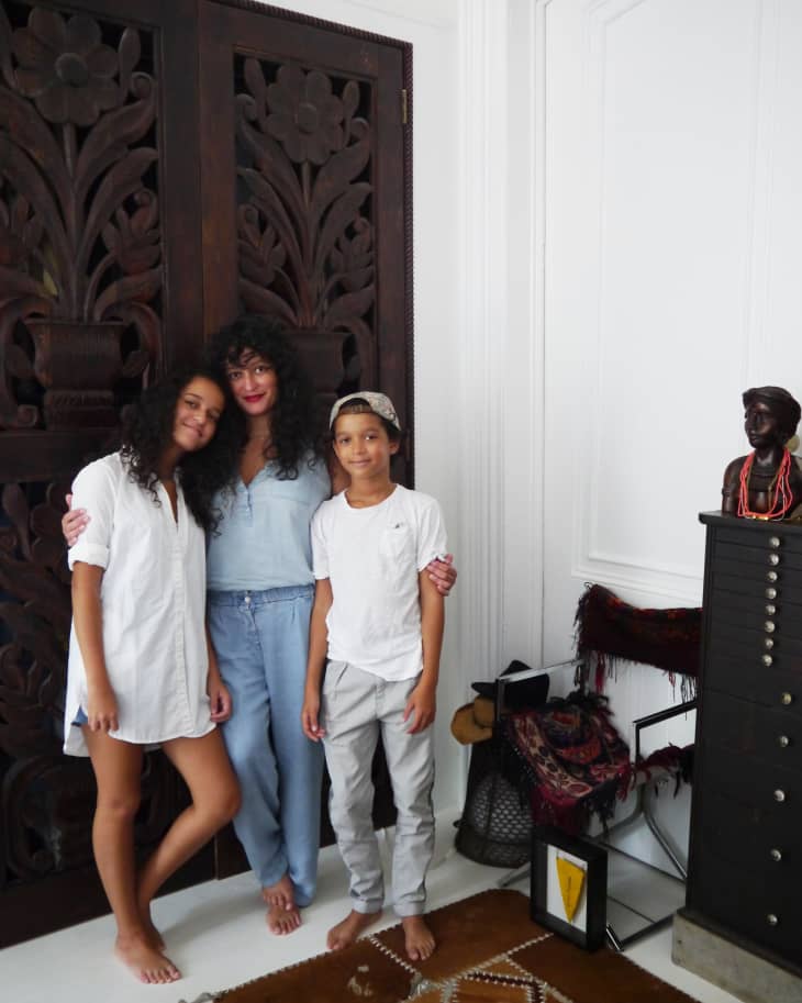 Family posing in front of carved wooden doors, with decorative items and a bust on a cabinet nearby.