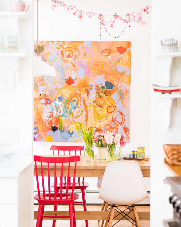Dining area with red chairs, abstract orange artwork, and a wooden table with flowers in vases.