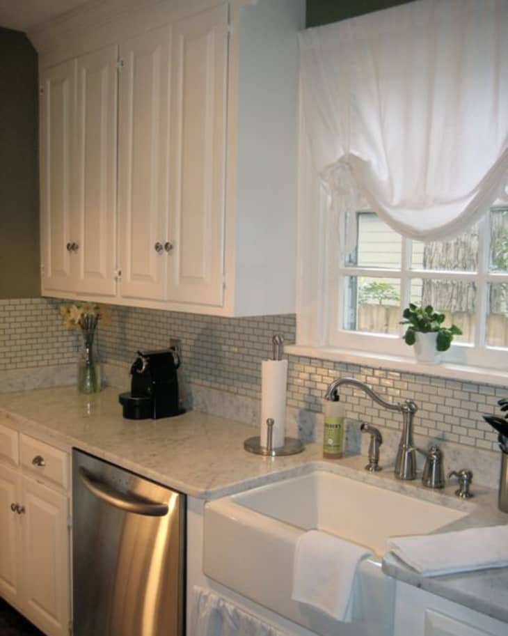 White kitchen with farmhouse sink, stainless steel dishwasher, white cabinets, and small tile backsplash.