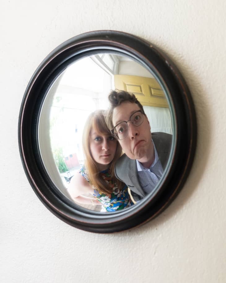 Two people making funny faces in a round wall mirror with a black frame.