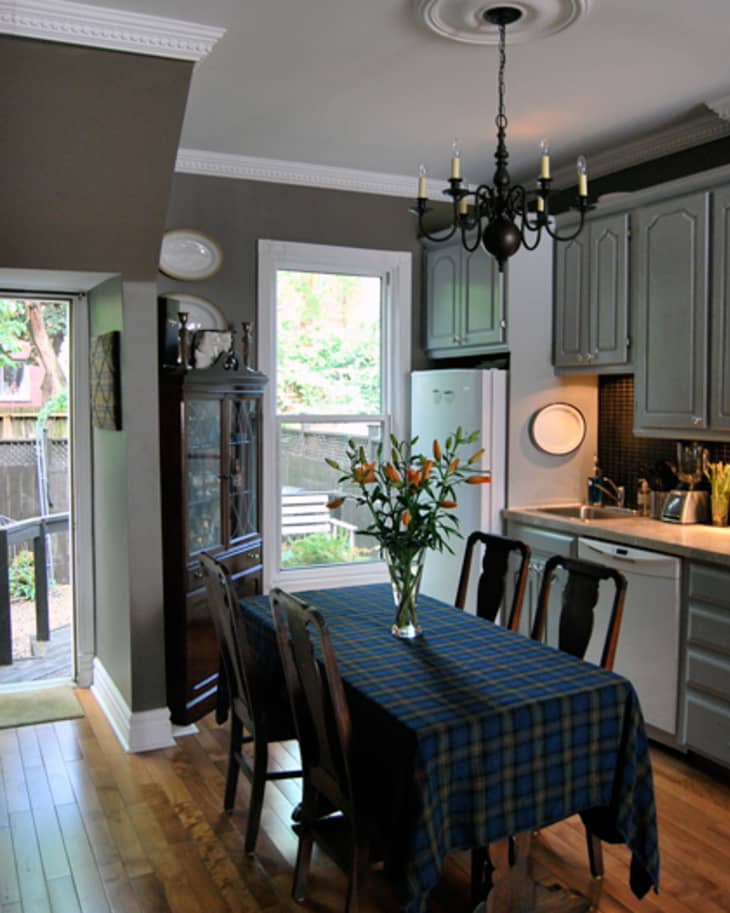 Dining room with a dark wood table, blue checkered tablecloth, vase of flowers, chandelier, and gray cabinets.