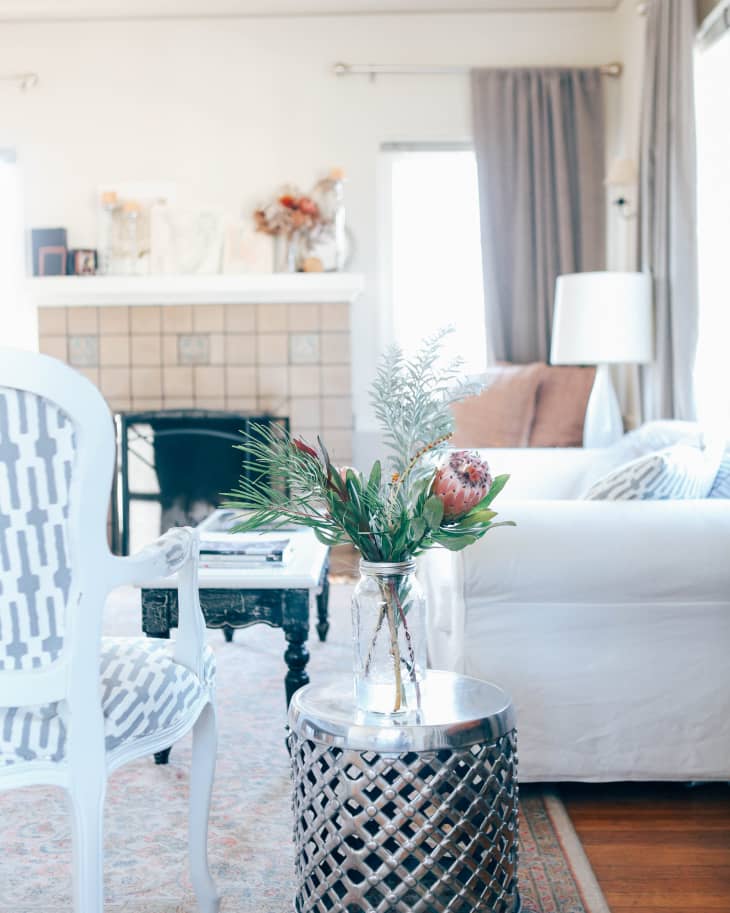 Living room with white sofa, patterned chair, metal side table, and vase of flowers, near a fireplace with decor.