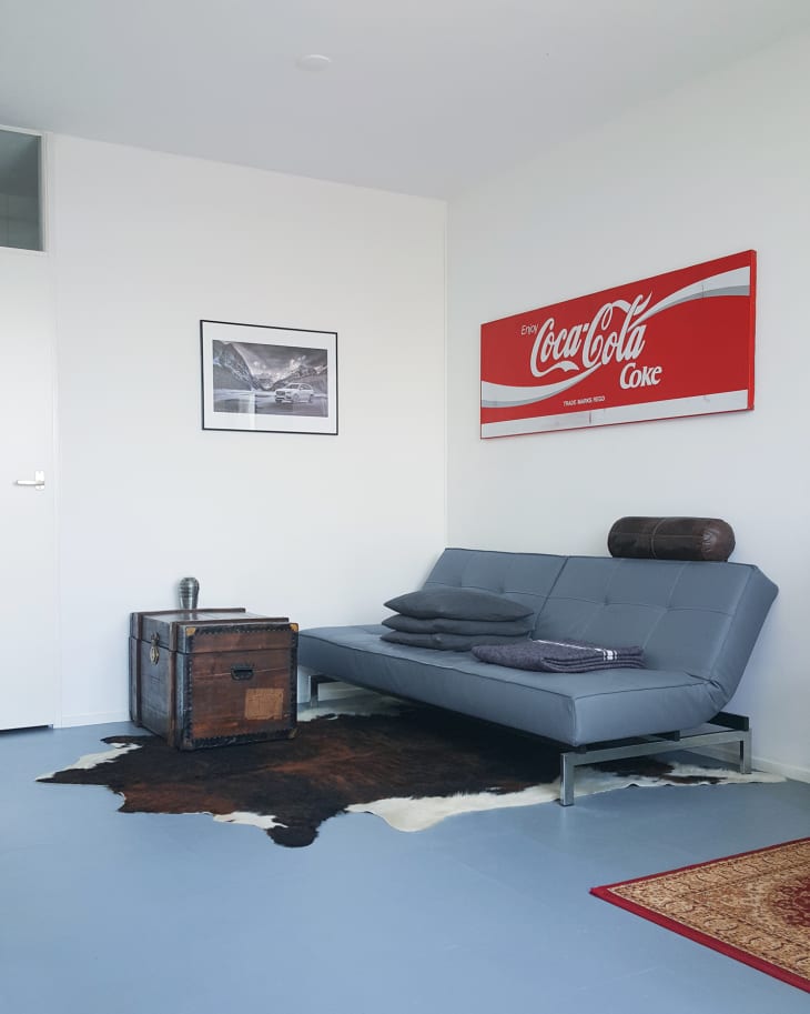 Modern living room with a gray futon, vintage trunk, cowhide rug, and Coca-Cola sign on the wall.