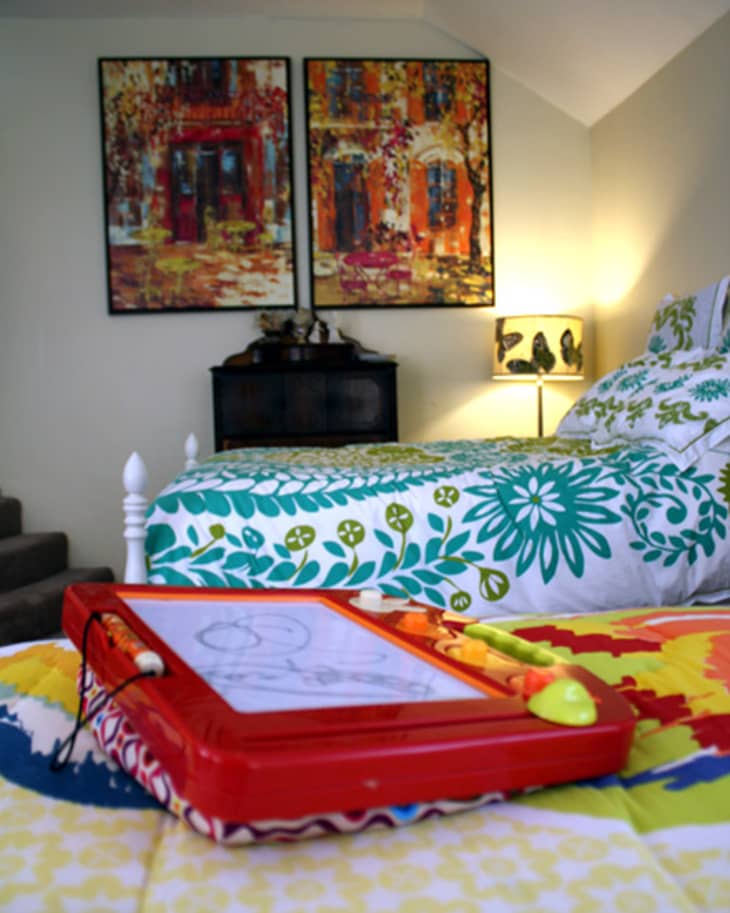 Colorful bedroom with floral bedding, abstract paintings, and a red drawing board on the bed.