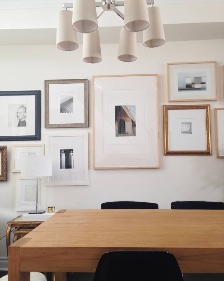 Dining room with wooden table, black chairs, gallery wall of framed art, and modern chandelier.